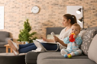 Evde çalışan anne süre kanepede oturan şirin bebek