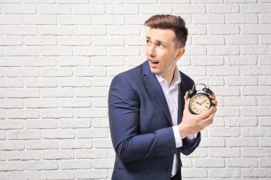 Sorunlu işadamı ile çalar saat beyaz duvara karşı. Zaman yönetimi kavramı