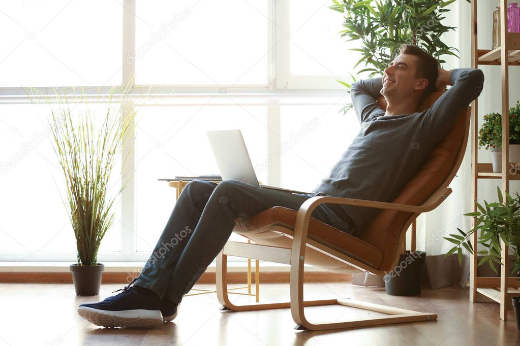 Young freelancer relaxing in armchair with laptop at home