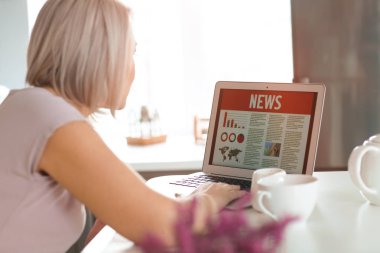 Olgun kadın evde laptop ekranında haber okuma