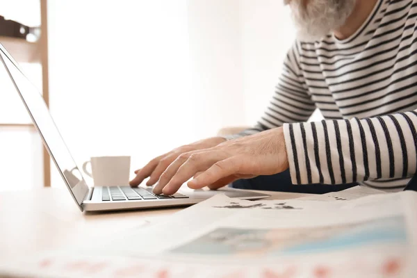 Senior man reading news on laptop screen at home