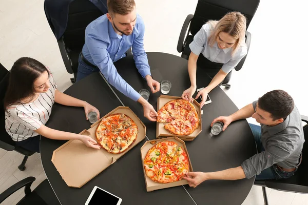 Young people eating pizza at table in office