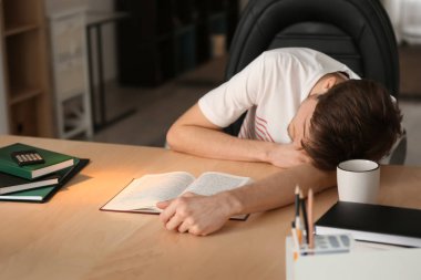 Genç adam kitap ile masada otururken uyuyor