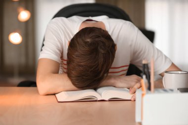 Genç adam kitap ile masada otururken uyuyor