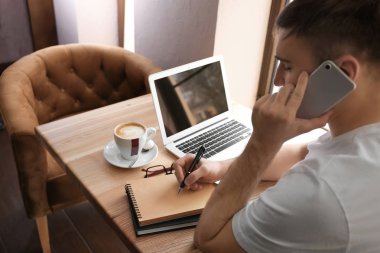 Kafede dizüstü bilgisayarda çalışırken cep telefonu üzerinde konuşurken genç serbest meslek