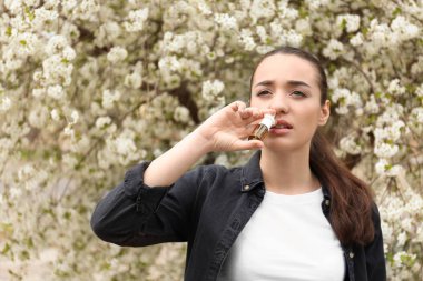 Çiçeklenme tree yakınındaki burun damlaları kullanan genç kadın. Anti kavramı