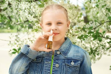 Little girl using nasal drops near blooming tree. Allergy concept clipart