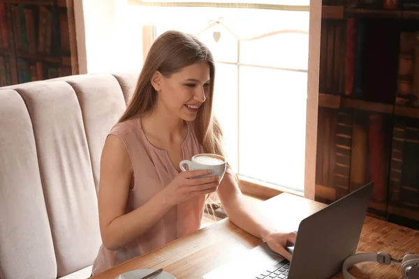カフェでノート パソコンでの作業中にコーヒーを飲む若いフリーランサー — ストック写真