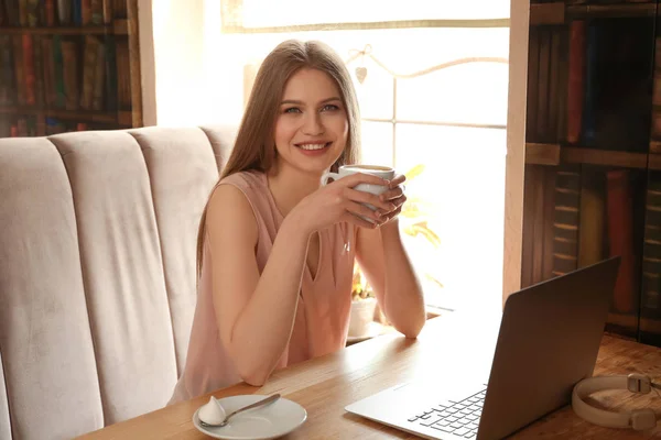 カフェでノート パソコンでの作業中にコーヒーを飲む若いフリーランサー — ストック写真