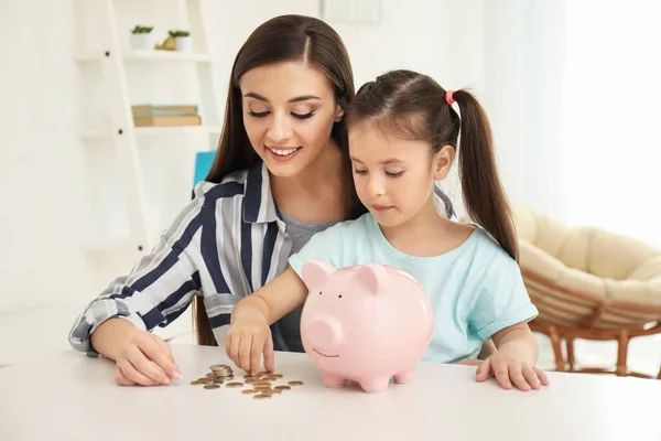 Niña Con Madre Sentada Mesa Poniendo Monedas Una Alcancía Interior —  Fotos de Stock