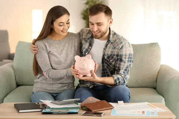 幸せなカップルの屋内で貯金箱を押しソファーに座っていた お金の節約のコンセプト — ストック写真