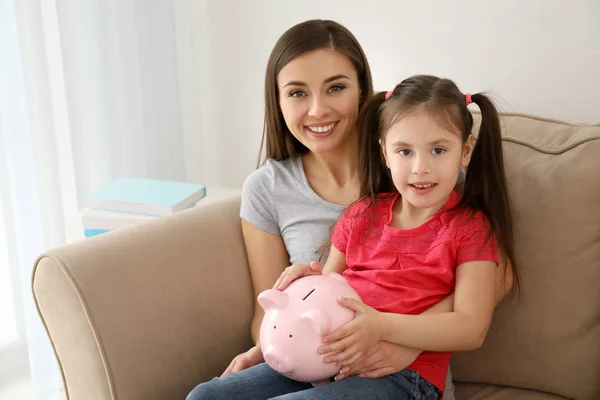 Little Girl Her Mother Sitting Sofa Holding Piggy Bank Indoors — Stock Photo, Image