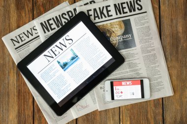 Gazeteler, tablet bilgisayar ve telefon ahşap masa üstünde perde haberleri ile