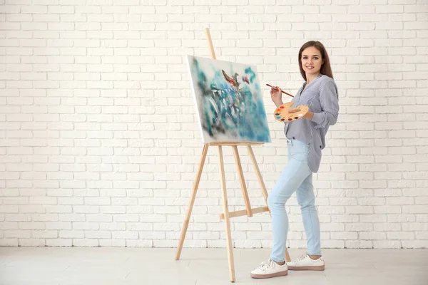 Young female artist with drawing easel against white brick wall
