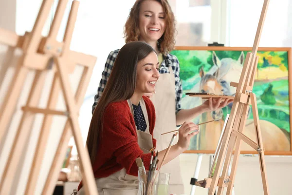 Female teacher helping her student during classes in school of painters