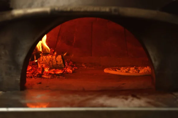 Oven with burning firewood and tasty pizza in restaurant kitchen