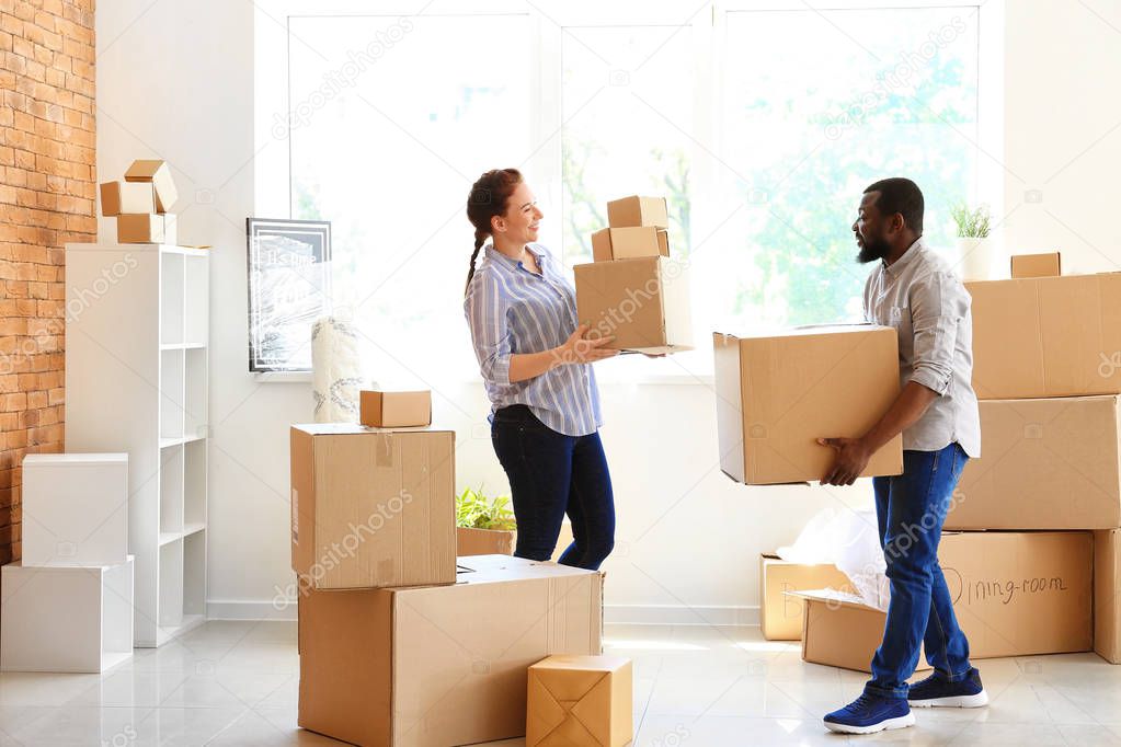 Interracial couple carrying boxes indoors. Moving into new house