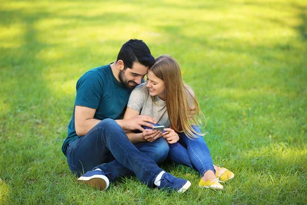 Glückliches Junges Paar Mit Handy Sitzt Auf Grünem Gras Park — Stockfoto