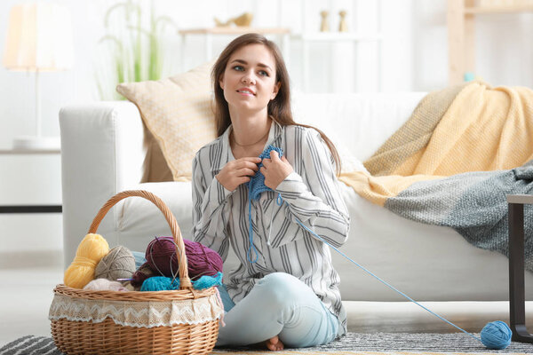 Young woman sitting on floor with knitting clothes at home