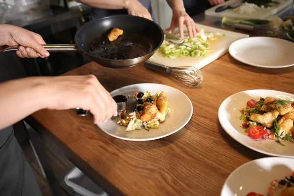 Jonge vrouw bereiden smakelijke vlees en salade tijdens kooklessen in restaurant keuken — Stockfoto