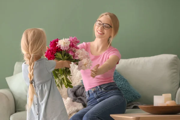 Cute little girl giving flowers to her mother at home