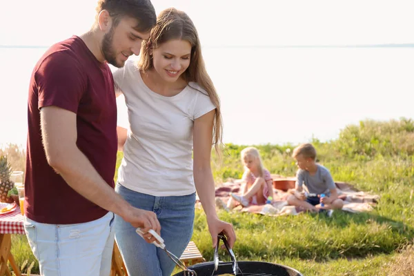 快乐的年轻夫妇烹饪美味的食物在烤肉烧烤户外 家庭野餐 — 图库照片
