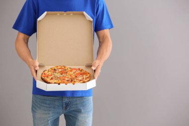 Gri arka plan üzerinde lezzetli pizza kutusu tutan genç adam. Gıda dağıtım hizmeti