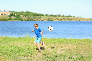 Sevimli çocuk futbol oynayan nehir kenarında