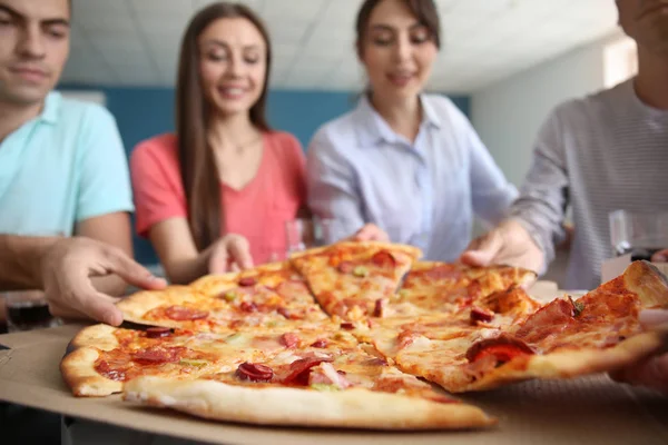 Young people taking slices of hot tasty pizza from cardboard box indoors
