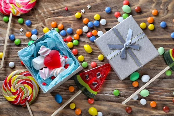 Composition with colorful candies and gift box on wooden background