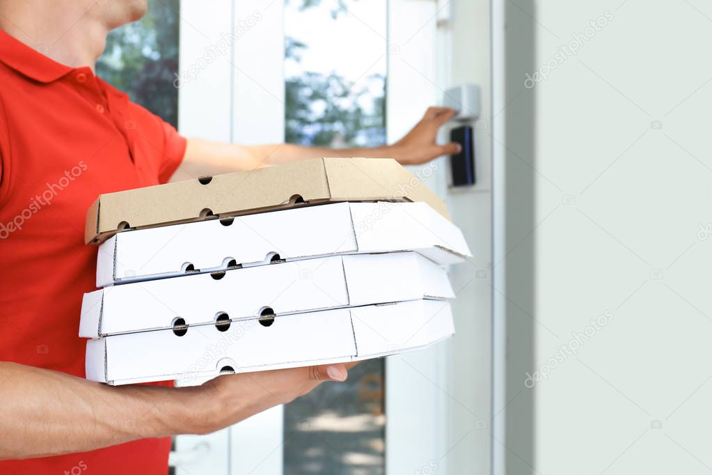 Young man with pizza boxes ringing the doorbell outdoors. Food delivery service