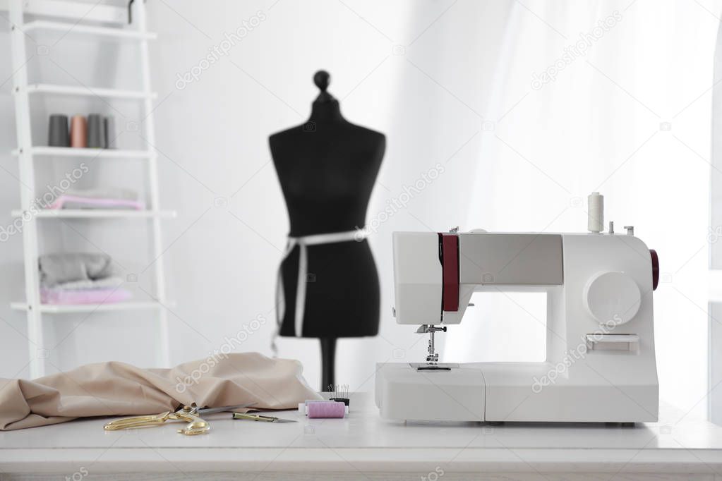 Modern sewing machine with fabric and tailor's supplies on table in workshop