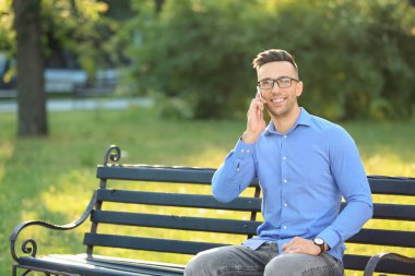 Yakışıklı adam cep telefonu üzerinde yeşil Park'ta dinlenme sırasında konuşurken