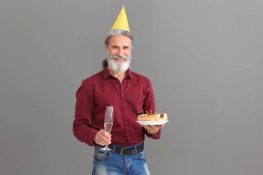 Doğum günü pastası ve şampanya gri arka plan üzerinde olan olgun adam