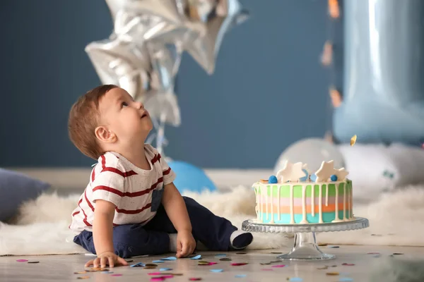 Cute little boy with birthday cake sitting on floor in room