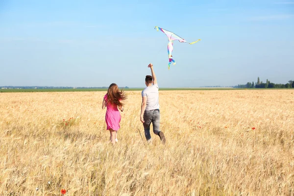 Happy young couple flying kite in a field