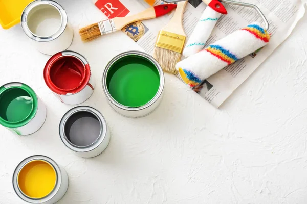 Paint cans with rollers and brushes on light background