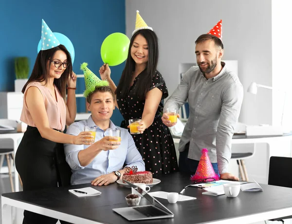 Young colleagues clinking glasses at birthday party in office