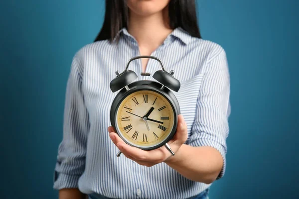 Woman holding alarm clock on color background. Time management concept