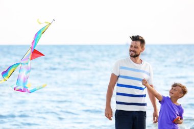 Baba ve oğlu deniz kenarında uçurtma ile