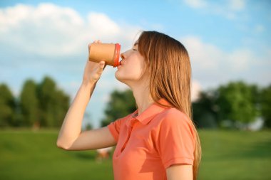 Genç kadın kahve parkta güneşli günde içme.