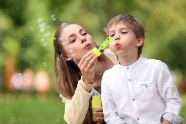 Mutlu anne ve oğlu parkta sabun köpüğü üfleme