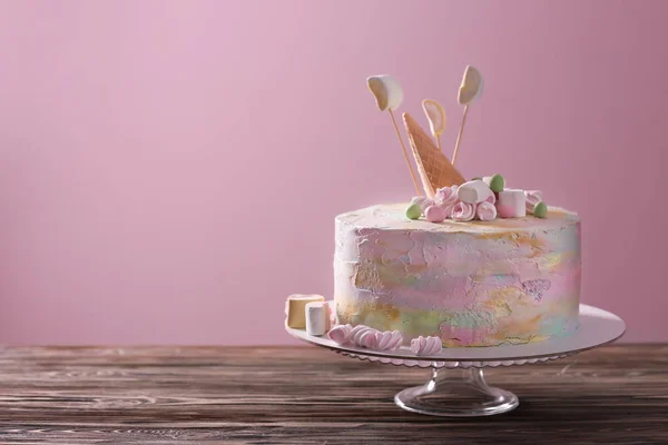 Stand with delicious birthday cake on table against color background