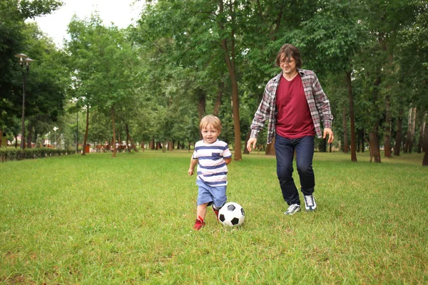 Happy father with son playing football in park on summer day