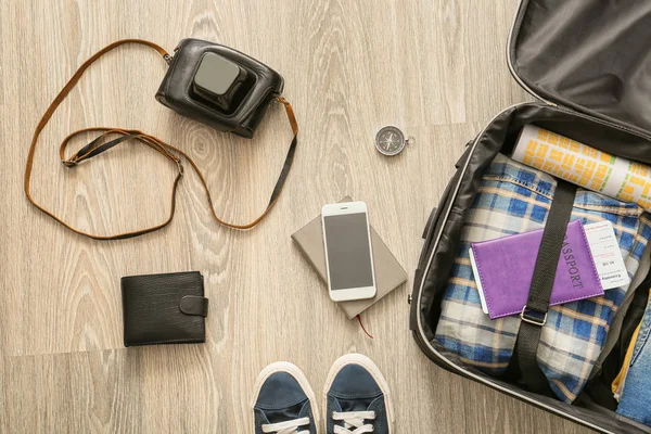 服でスーツケースを開き 木製の背景に旅行用品 — ストック写真