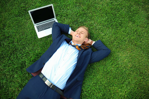 Young man in formal clothes relaxing on green grass outdoors