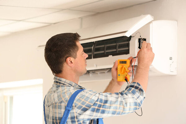 Electrician measuring voltage of air conditioner indoors