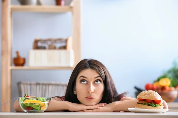 在室内有美味的汉堡和新鲜沙拉的女人 健康与不健康食品的选择 — 图库照片