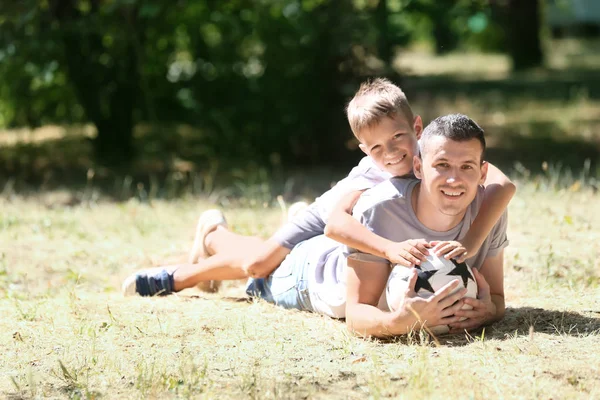 Mały Chłopiec Jego Tata Piłki Nożnej Leżąc Trawie Zewnątrz — Zdjęcie stockowe