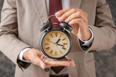 Gri arka plan üzerinde closeup çalar saat tutan bir iş adamı. Zaman yönetimi kavramı